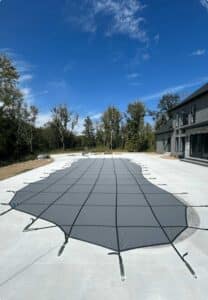 Seasonal pool cover shown completely covering a pool, in a sunny residential backyard setting.