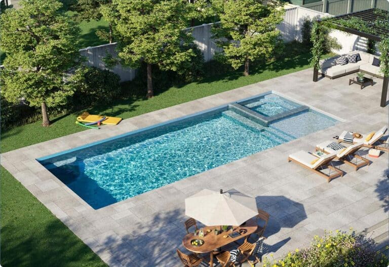 Rectangular fiberglass pool with clear water and stone decking in a backyard with trees.