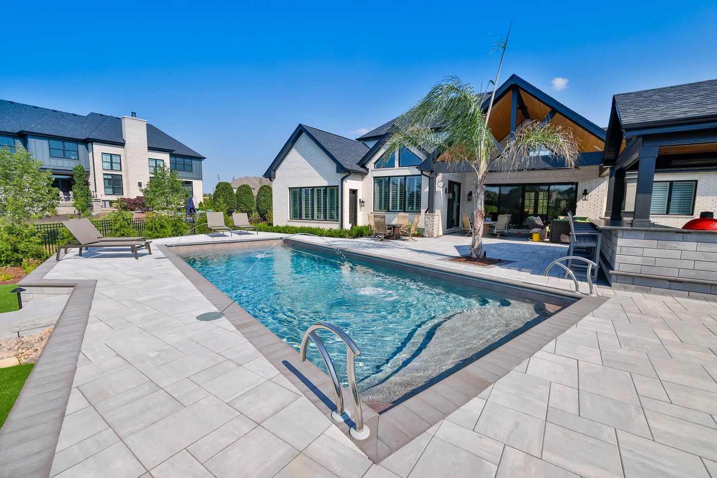 Spacious rectangular fiberglass pool with steps and tanning ledge beside a modern home.