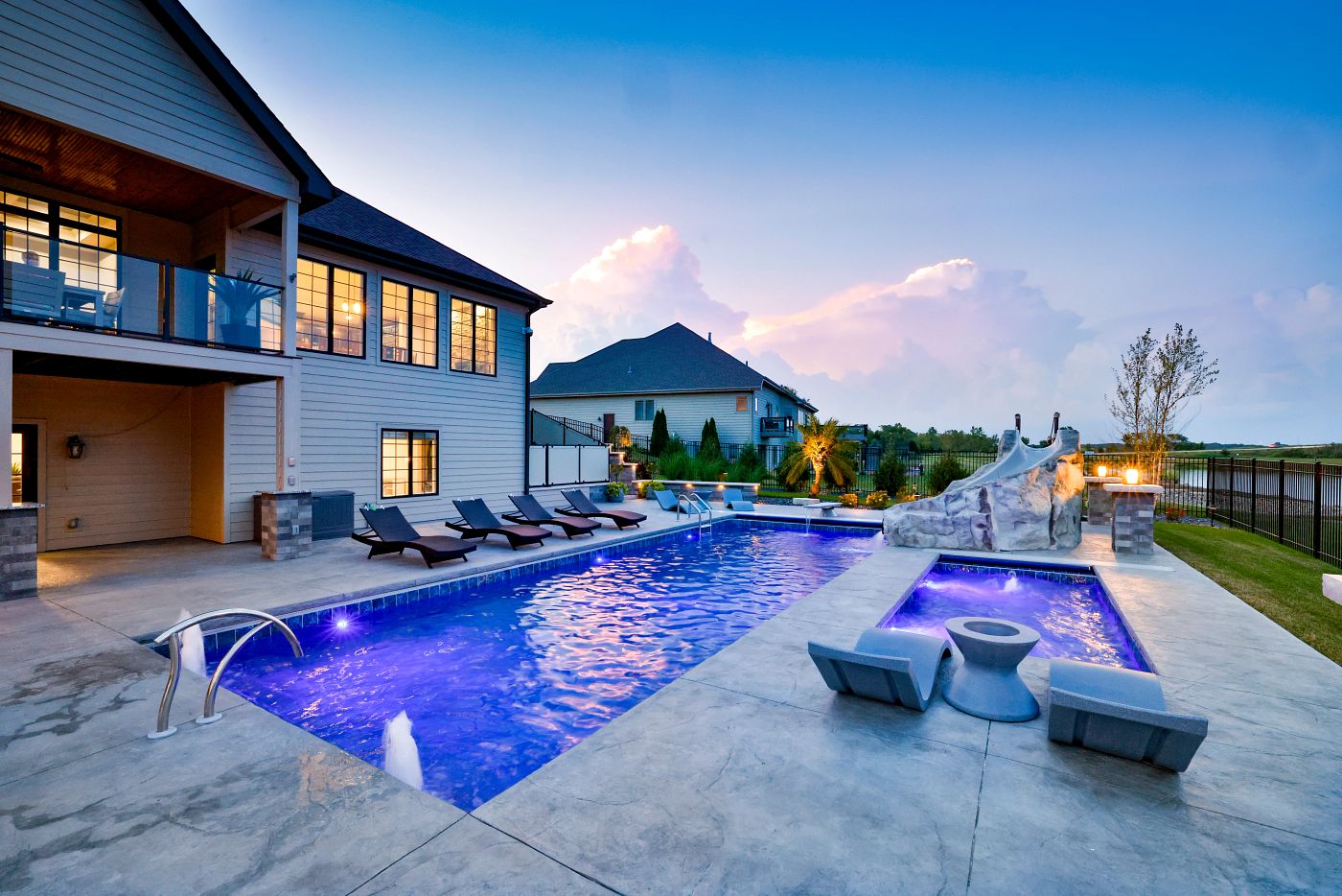 Large rectangular fiberglass pool with a connected tanning ledge, illuminated at night with vibrant blue LED lighting.