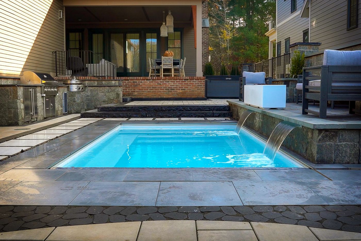 Compact rectangular plunge pool installed inground with stone coping and a waterfall feature in a small yard.