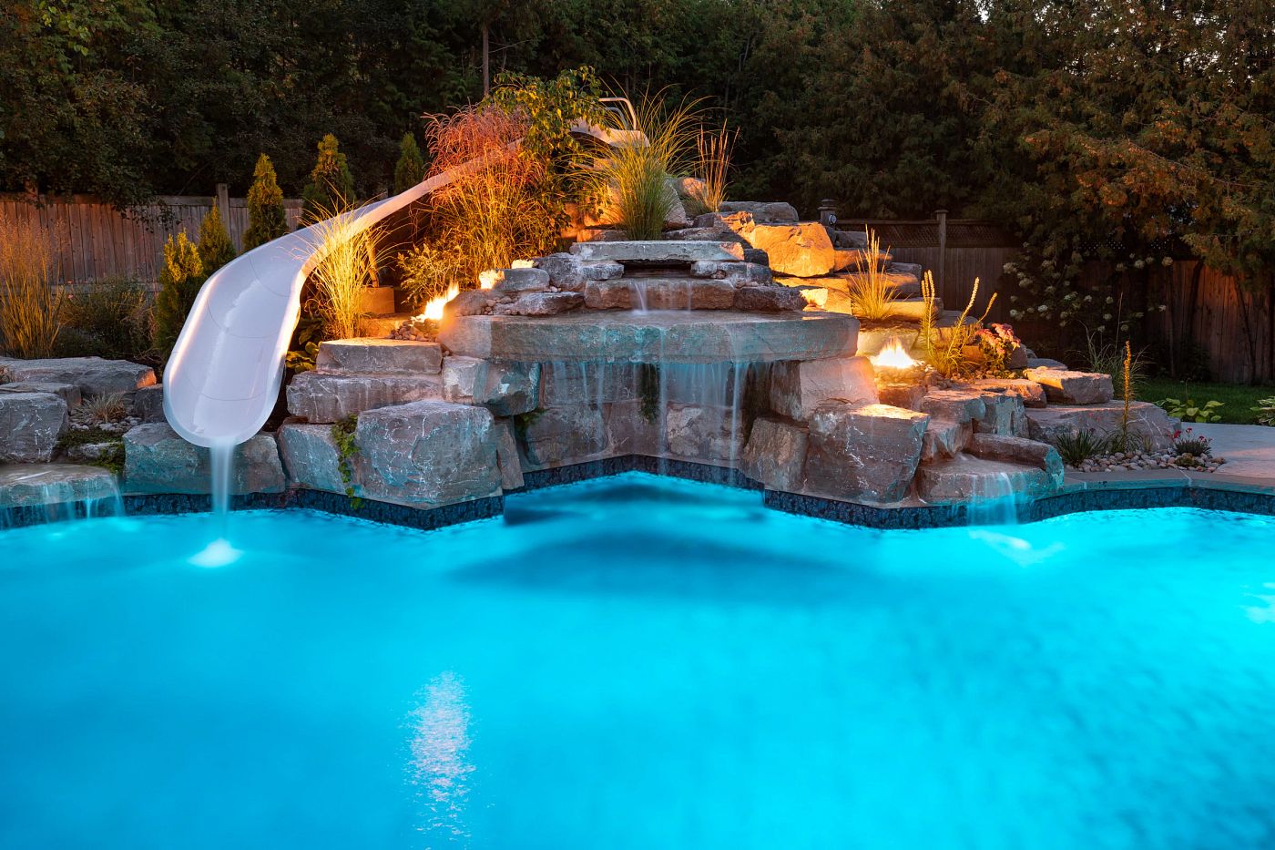 Vinyl liner pool featuring a dramatic rock waterfall, boulder landscaping, and a built-in water slide.