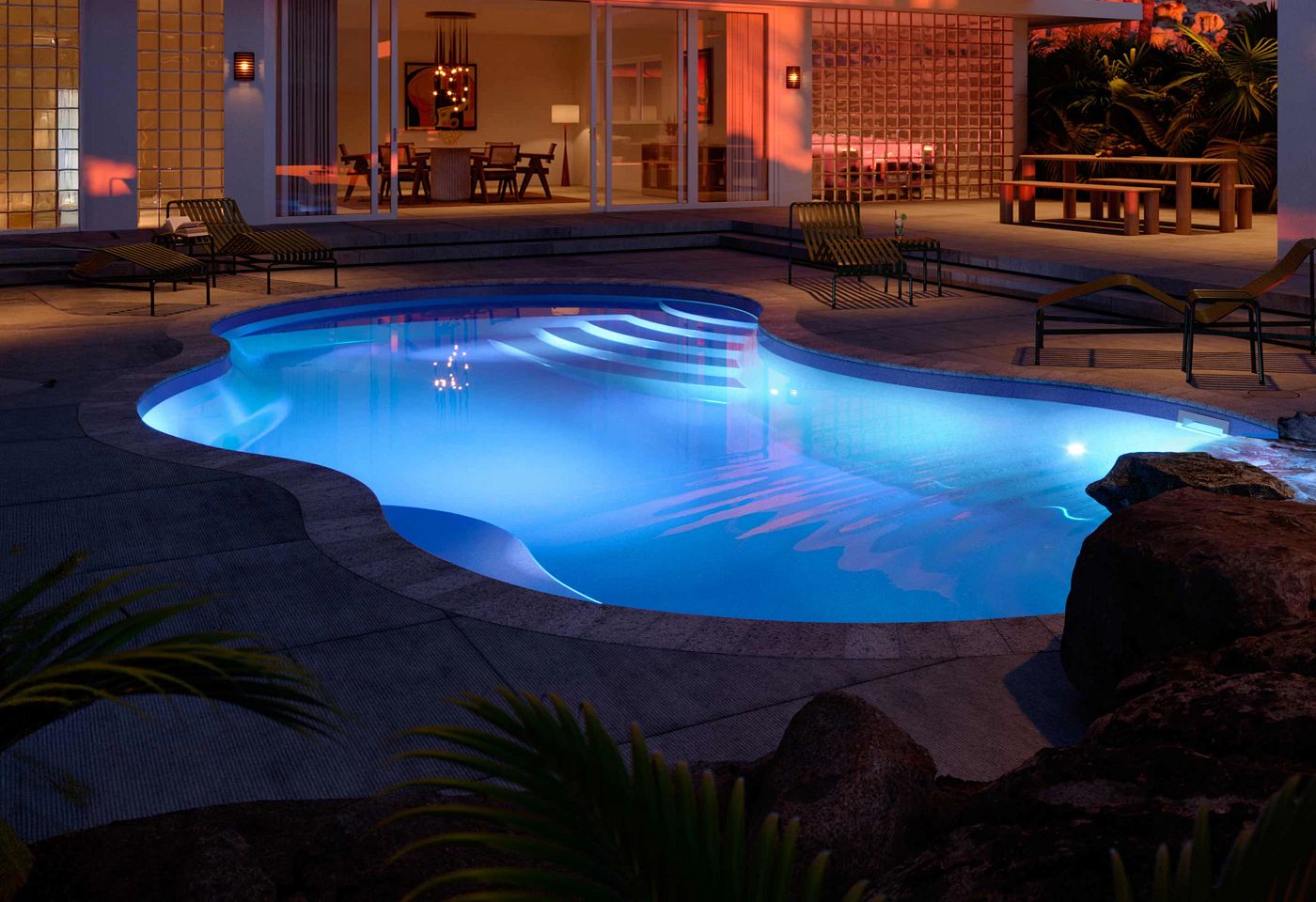 Freeform Coral 16 Latham fiberglass pool shown at night with vibrant blue underwater LED and patio lighting.